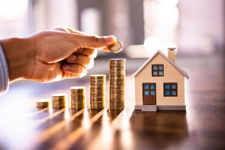 Une main plaçant une pièce de monnaie sur une pile de pièces, symbolisant l’accumulation progressive de capital.